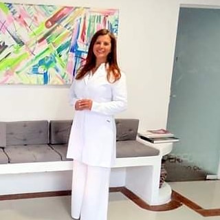 Dra. Eliana em pé, de jaleco branco, no consultório.