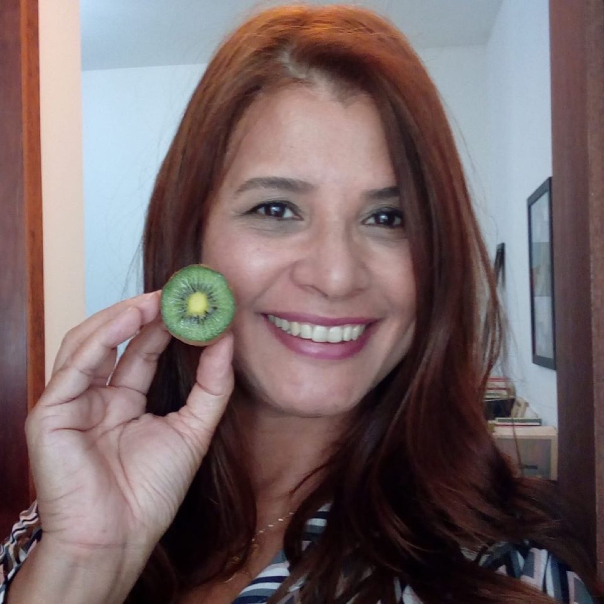 Dra. Eliana sorri segurando uma fatia de kiwi ao lado do rosto.