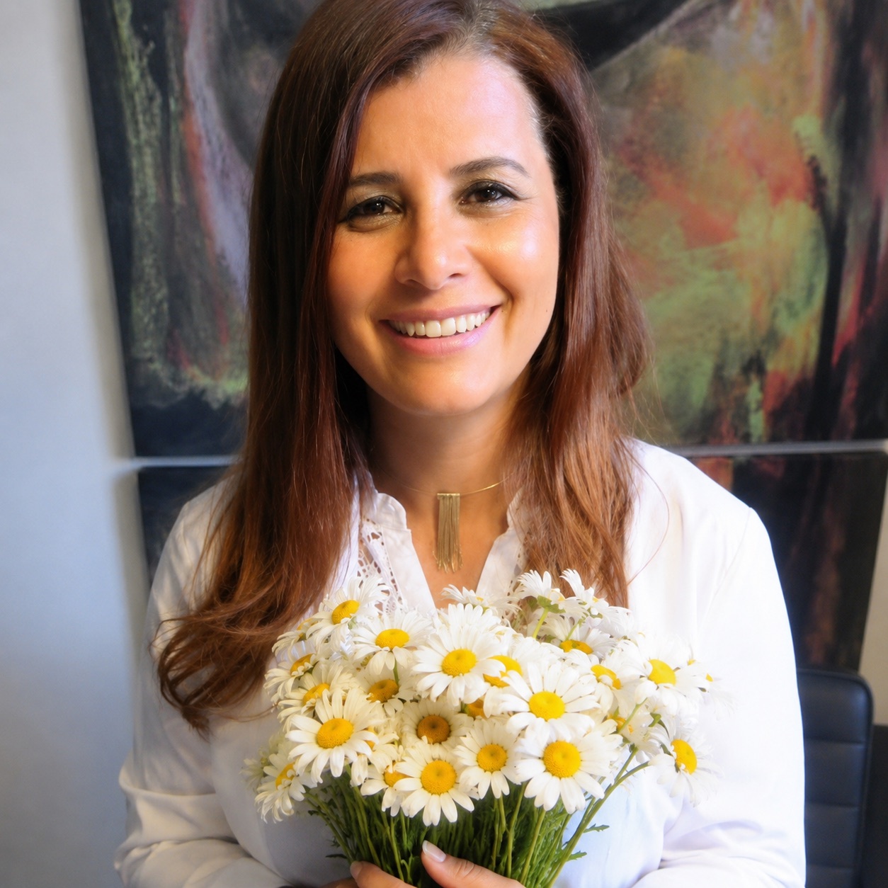 Dra. Eliana sorri segurando um buquê de flores brancas.